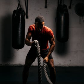 A man in a gym working out with ropes.