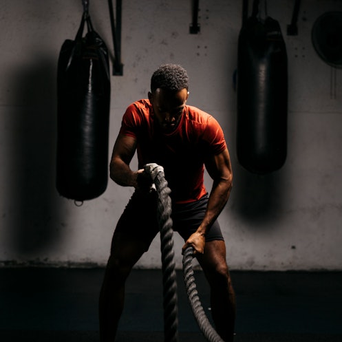 A man in a gym working out with ropes.