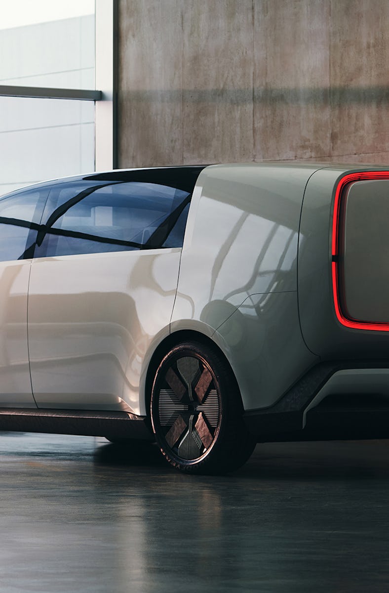 A futuristic electric vehicle with a boxy design and a red illuminated rear panel is parked in a mod...