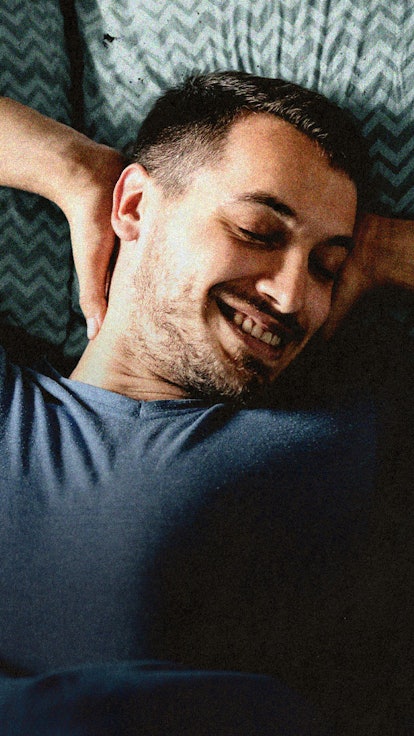 A man lying in bed, smiling, with his hands behind his head.