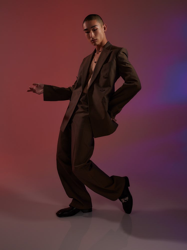 Model Sang Woo Kim wears a brown suit, necklace and black shoes.