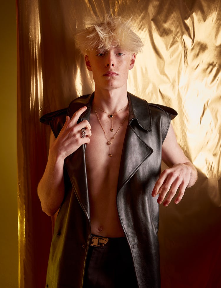 Model Ned Sims wears a leather vest and pants; gold string tangling necklace and ring.