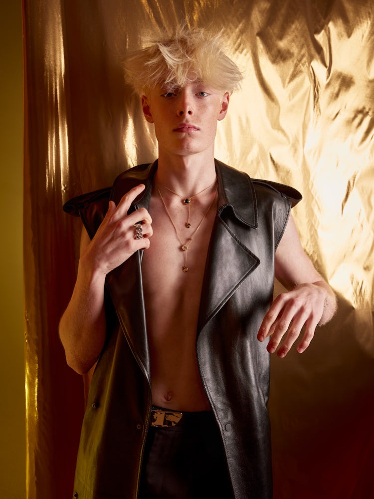 Model Ned Sims wears a leather vest and pants; gold string tangling necklace and ring.