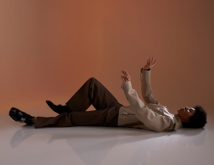 Model Kai-Isaiah Jamal wears a beige jacket, brown pants, ring, and black shoes.