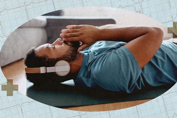 A man practicing yoga nidra, lying on a yoga mat on his living room floor, wearing headphones.