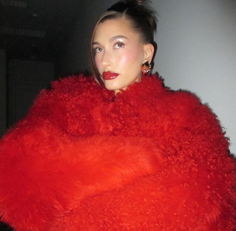 Hailey Bieber wears a red Ferragamo fur coat at the Rhode Skin holiday office party