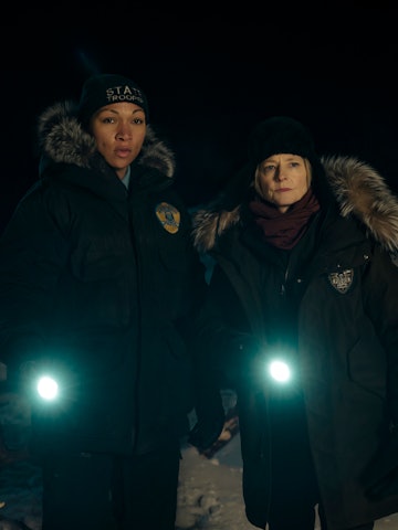 Two women with flashlights stand outside at night in winter clothing near a canvas tent with a snowy...