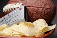 A football rests in a bowl of chips with a remote control, representing a Super Bowl party.