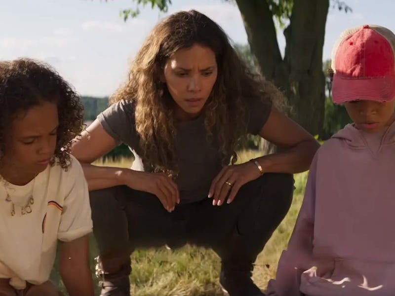 A woman crouching between two children looks intently ahead, the kids appear concerned against a rur...