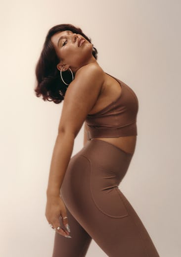 A woman poses confidently in a brown activewear outfit against a neutral background.