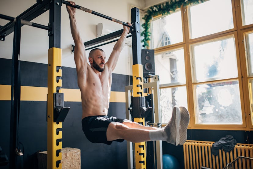 A man doing a hanging leg raise in a home gym.