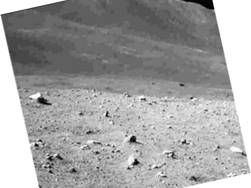 Boulders and gravel cover the ground, and a ridge rises behind it. Farther away, the blackness of sp...
