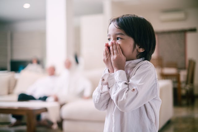 A little boy holds his hands over his mouth.