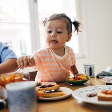 A toddler eats dinner of toast and toppings.