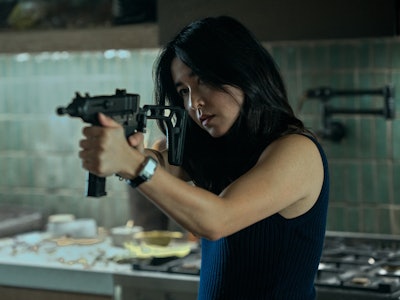 A person aiming a gun with focus, standing in a kitchen with tile walls and a blur of kitchenware in...