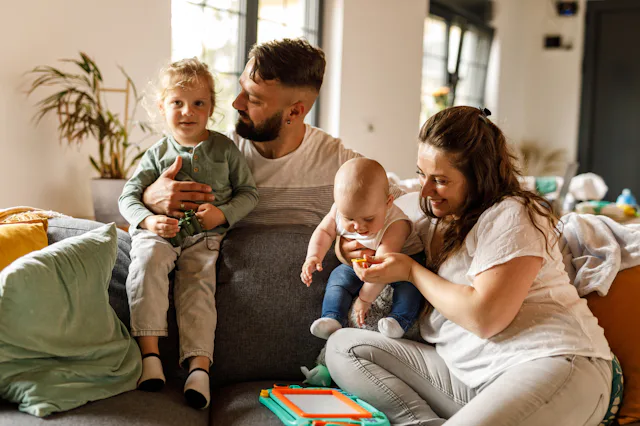 A family sits on the couch with their young kids.