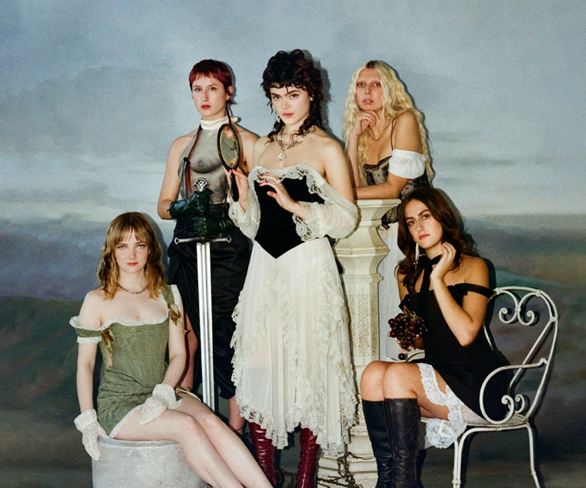 Five women in vintage clothing posing in a classical painting style with a muted background.