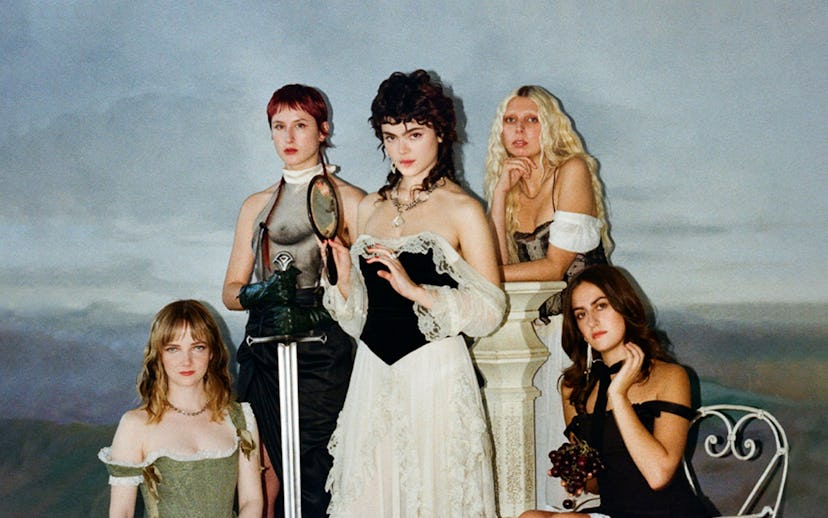 Five women in vintage clothing posing in a classical painting style with a muted background.