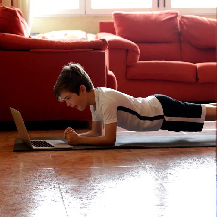 A young boy holds a plank while exercising.
