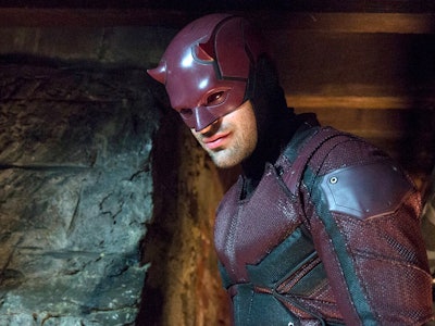 Man in a red superhero costume with a masked helmet, standing in a dimly lit, underground setting.