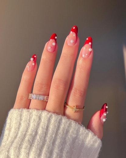 Pontas francesas vermelhas com adornos de pérolas são uma ideia moderna de manicure francesa para 2024.