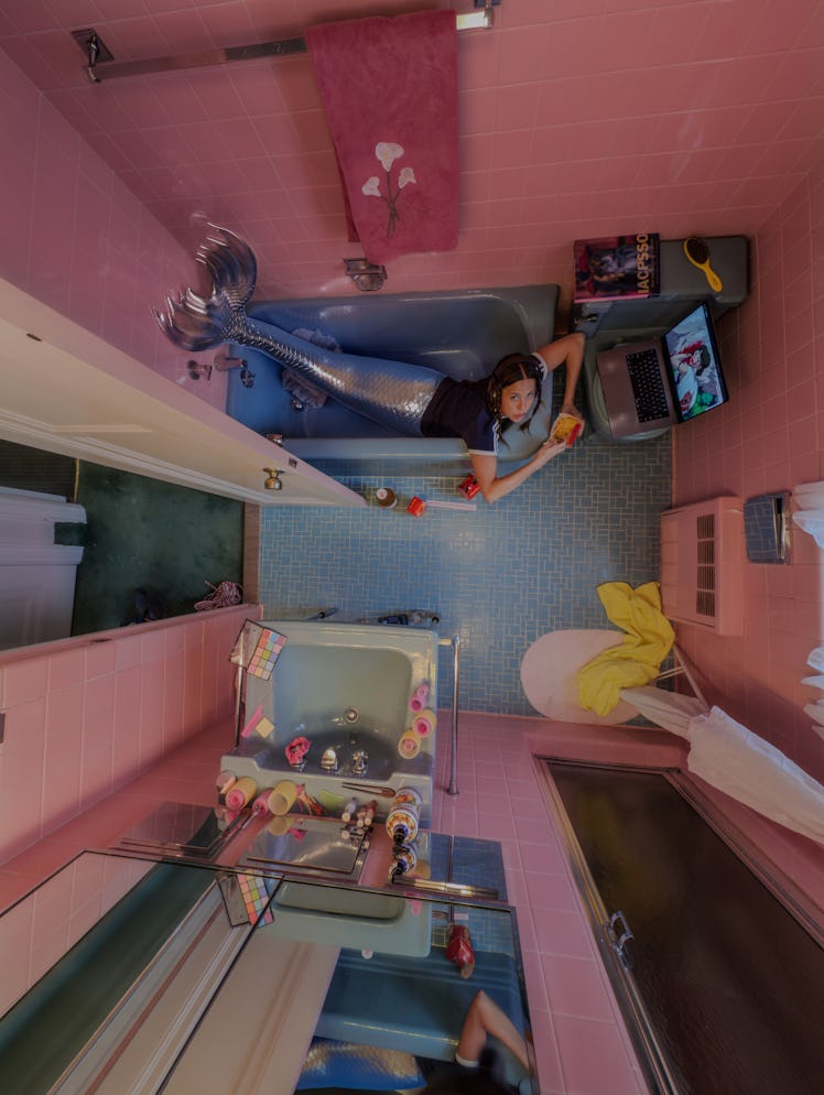 a bird's eye view photograph of a person in a bathroom with pink walls and a sky blue bathtub and ti...