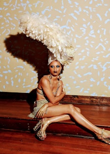 a person sitting on a step with a big cream colored feathered headdress