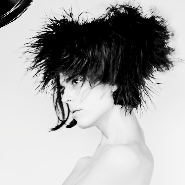 a blurry black and white photograph of someone wearing a feather hat that blends with their black ha...