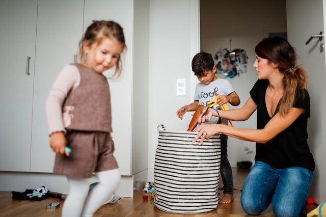 A mother helps her kids pick up toys.