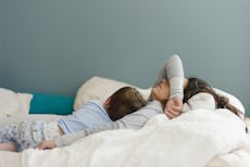 A woman who isn't feeling well lays in bed with her child.