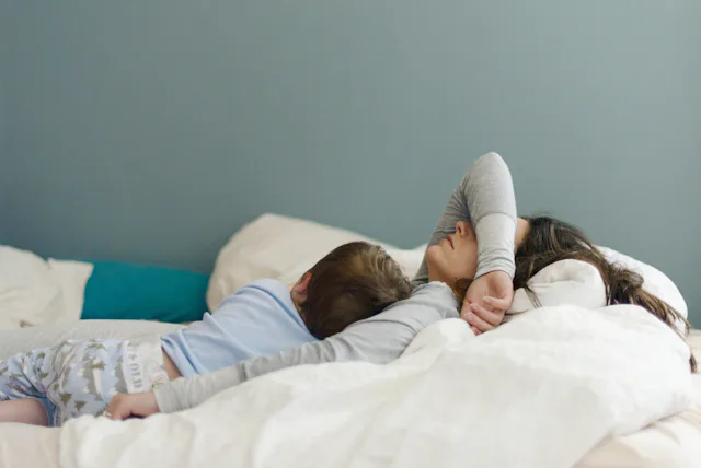 A woman who isn't feeling well lays in bed with her child.