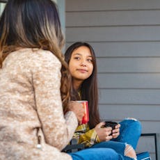 A mother and her daughter talk on the porch.