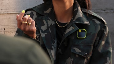 L'Ai Pin avec une manche jaune attachée à une veste camouflage.