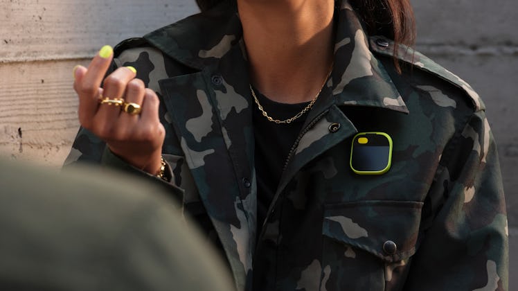 The Ai Pin with a yellow sleeve attached to a camo jacket.