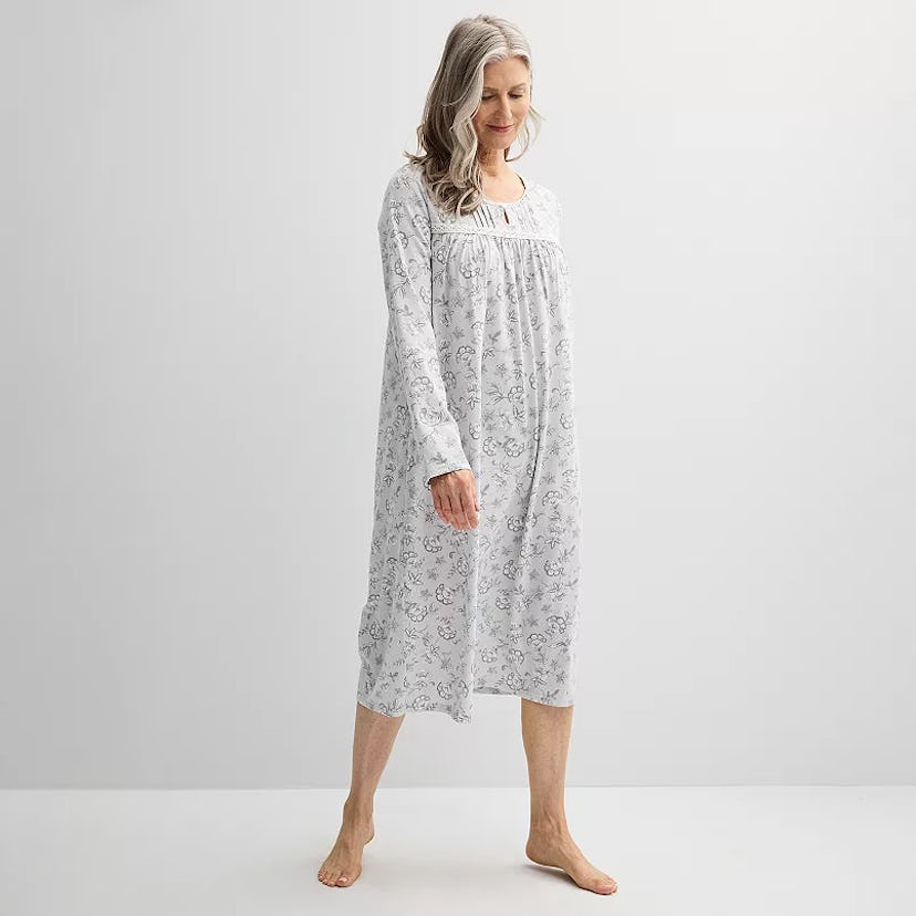 A woman with long gray hair is wearing a long, light gray nightgown with a floral pattern. She stand...