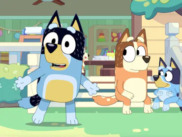 Three cartoon dogs are outside a colorful house. The blue dog with a black patch talks animatedly, w...