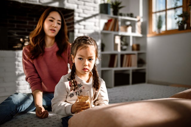 A woman and a young girl sit together in a cozy, well-lit room. The girl holds a drink while the wom...
