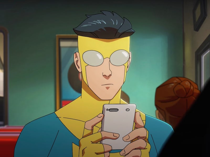 A young man wearing a bright yellow superhero costume and glasses sits in a diner, focused on his sm...