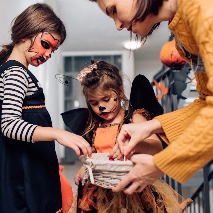 Two children in Halloween costumes explore a basket with treats. One has a striped outfit and face p...