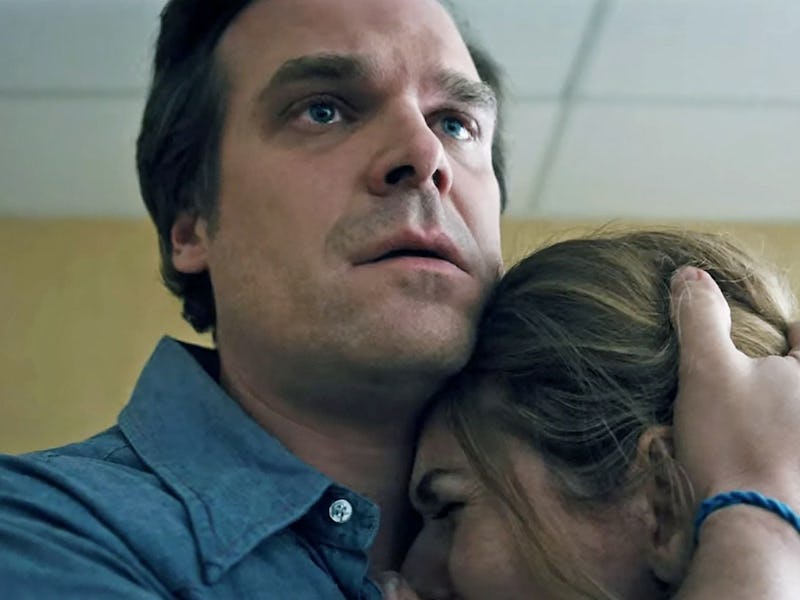 A man looks concerned while holding a woman close, who appears to be crying. They are in a dimly lit...