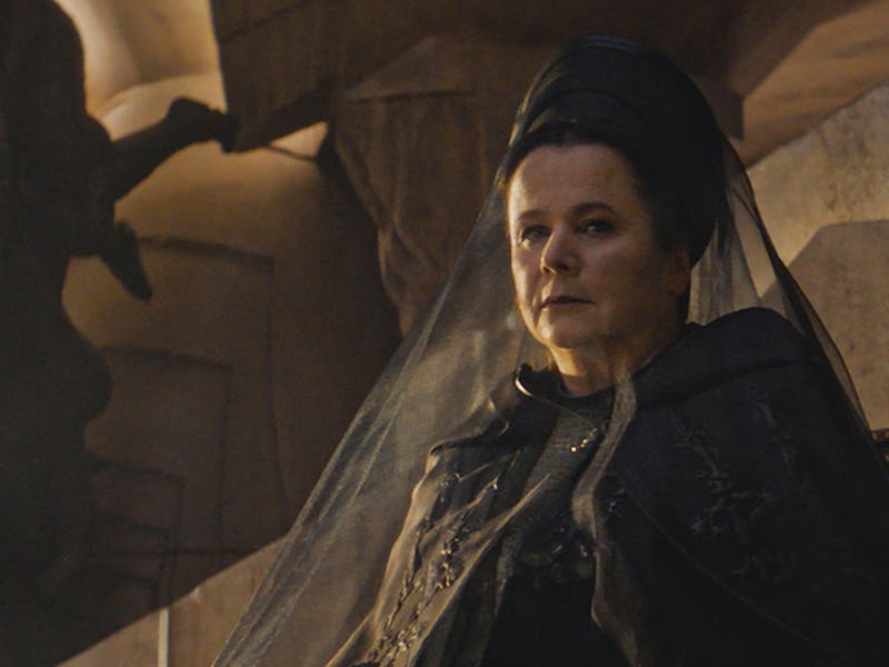 A woman in a dark, ornate outfit sits regally, wearing a veil and looking thoughtfully into the dist...