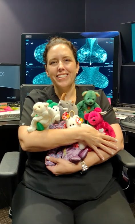 A smiling woman in scrubs sits in an office, holding a collection of colorful stuffed animals. Monitors displaying medical imagery are visible behind her.