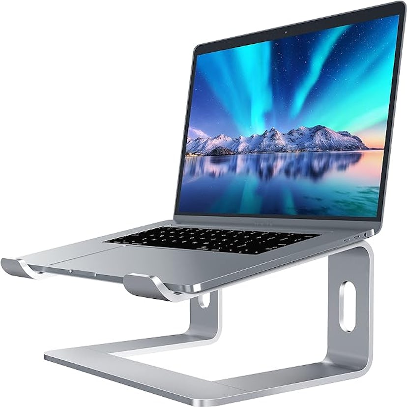 A sleek silver laptop stand holds a laptop at an angle, featuring a scenic screen display of mountai...