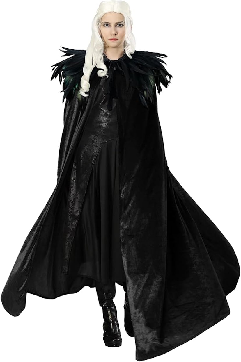 A woman in a dramatic black costume with a long, flowing cape and feathered collar stands confidentl...