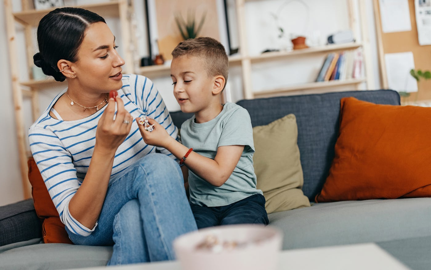 A mother and her young son share a moment on a sofa, smiling and interacting playfully while enjoying snacks in a cozy living room.