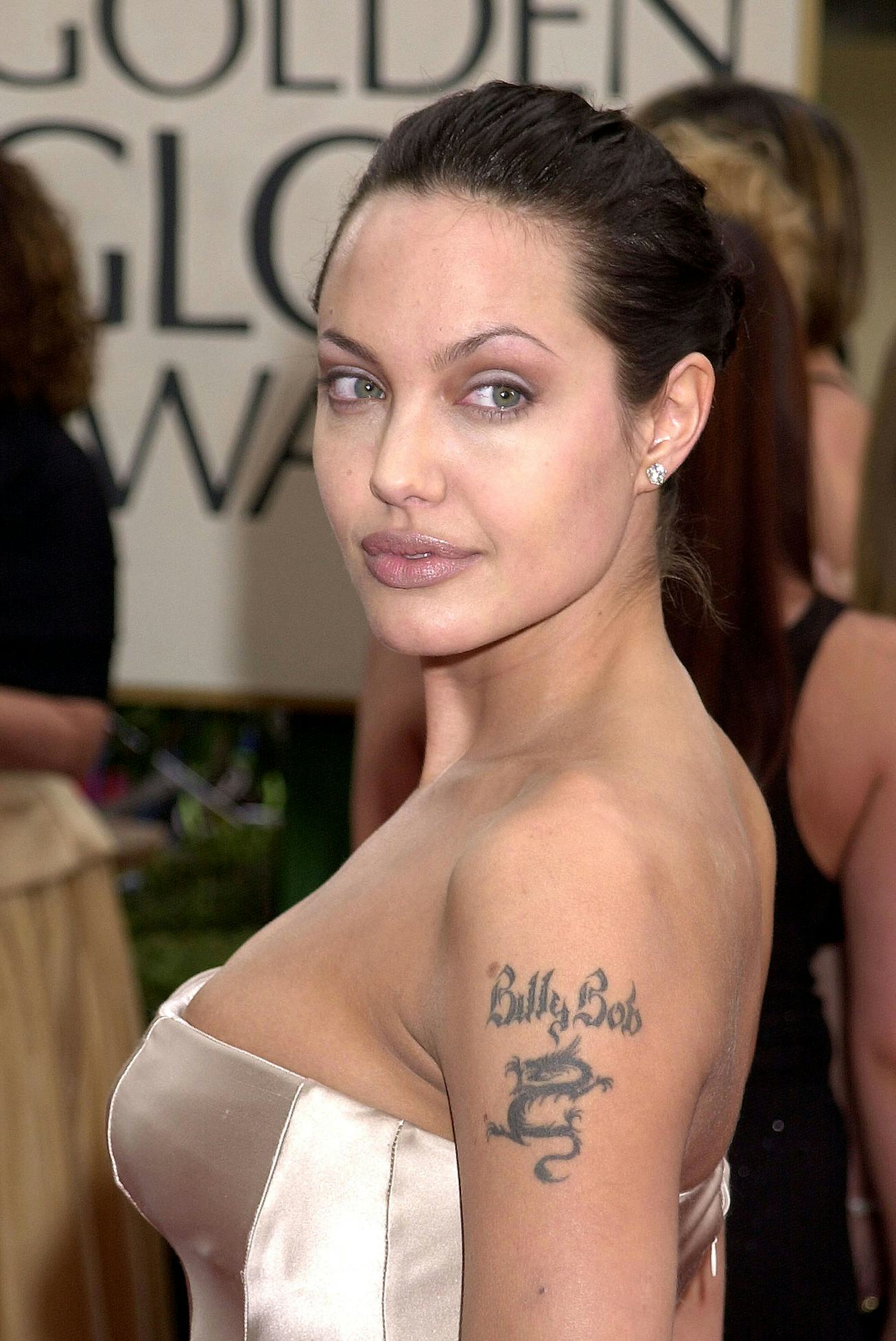Angelina Jolie in sleek bun wears a strapless, light dress, showcasing a tattoo on her arm