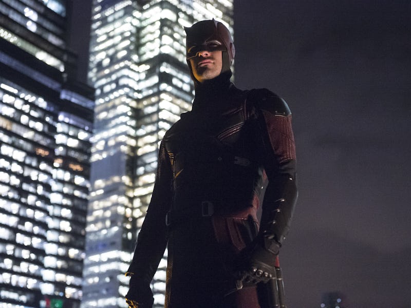 A superhero in a dark, sleek costume stands confidently on a rooftop with a city skyline and illumin...