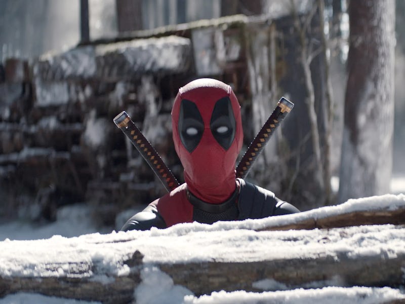 A masked figure in a red and black costume with two katanas peeks over a snow-covered log in a fores...