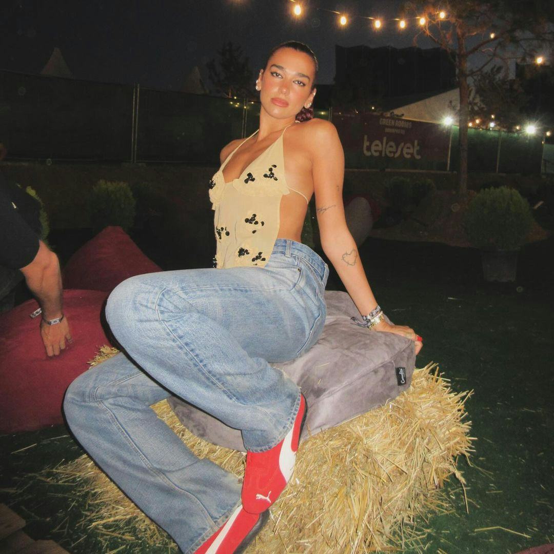 Dua Lipa wears a yellow halter top, jeans, and red PUMA Speedcats.
