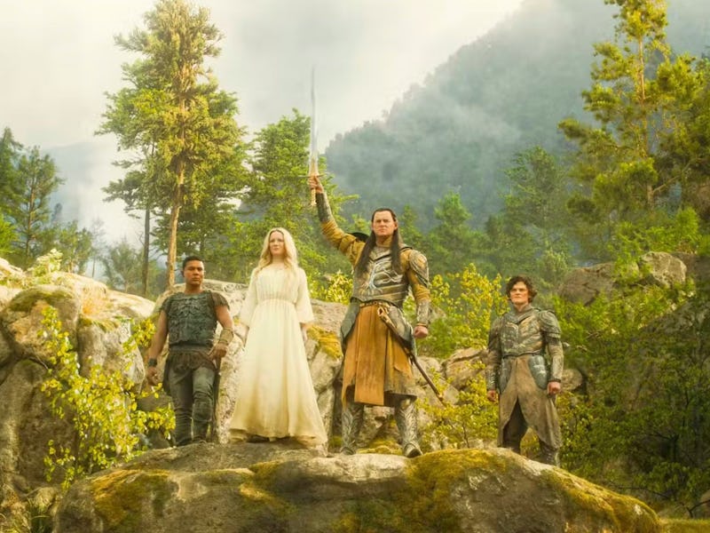 Four characters stand on a rocky outcrop, surrounded by lush greenery and mountains. One holds a swo...